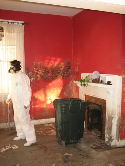 Worker in a white protective suit and respirator standing in a room with moldy red walls